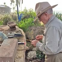 Man in a tan hat and gray shirt using a small tool at an outdoor stone work area