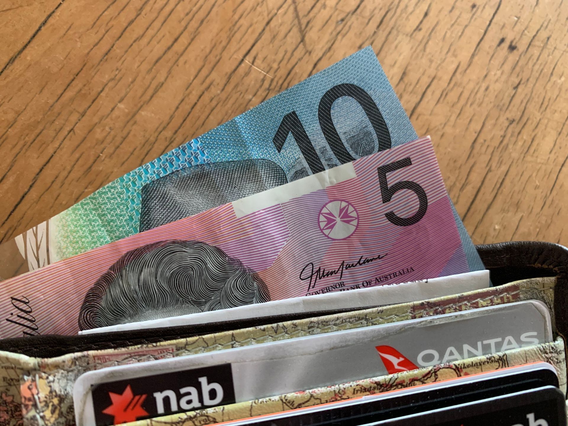 Australian banknotes sticking out of a wallet on a wooden surface.