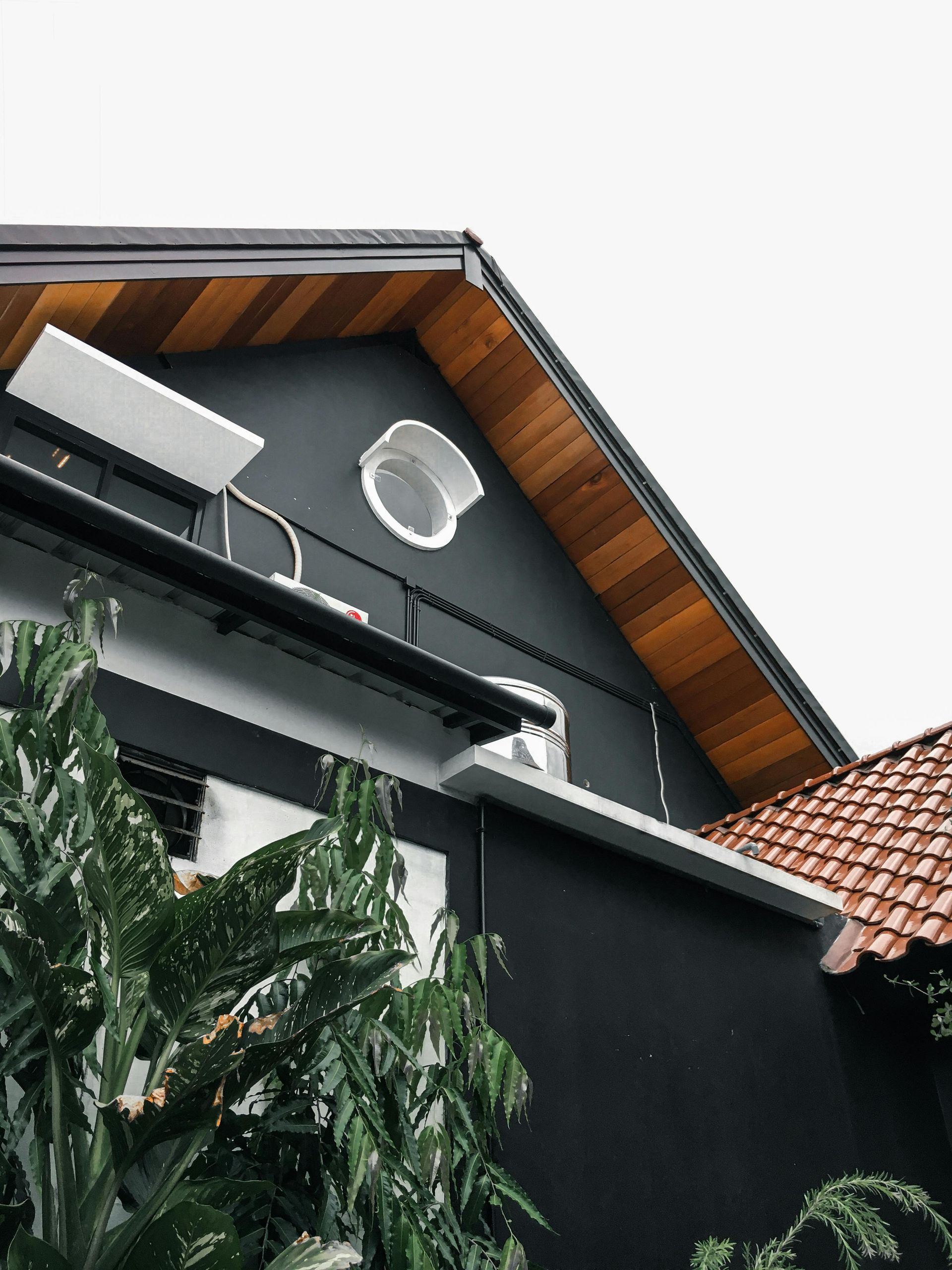 Black building with brown roof eaves, round window, and air conditioning unit.