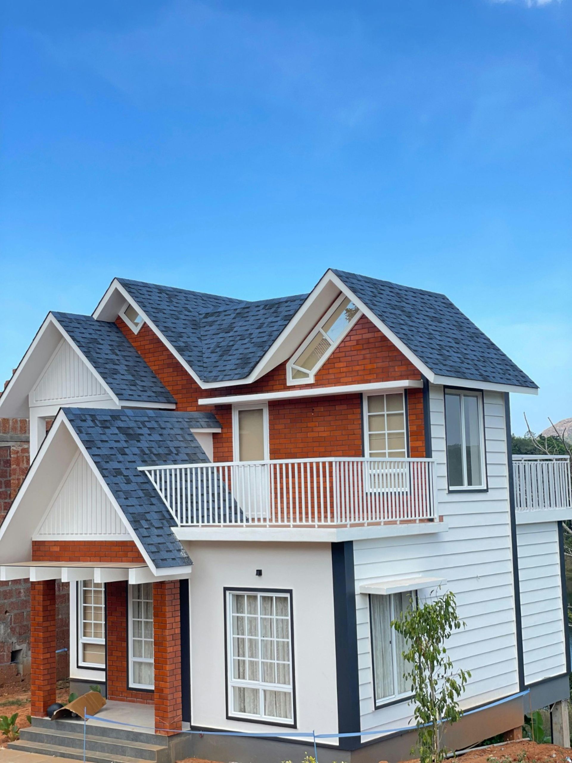 Two-story house with dark blue roof, white siding, and red brick accents against a blue sky.