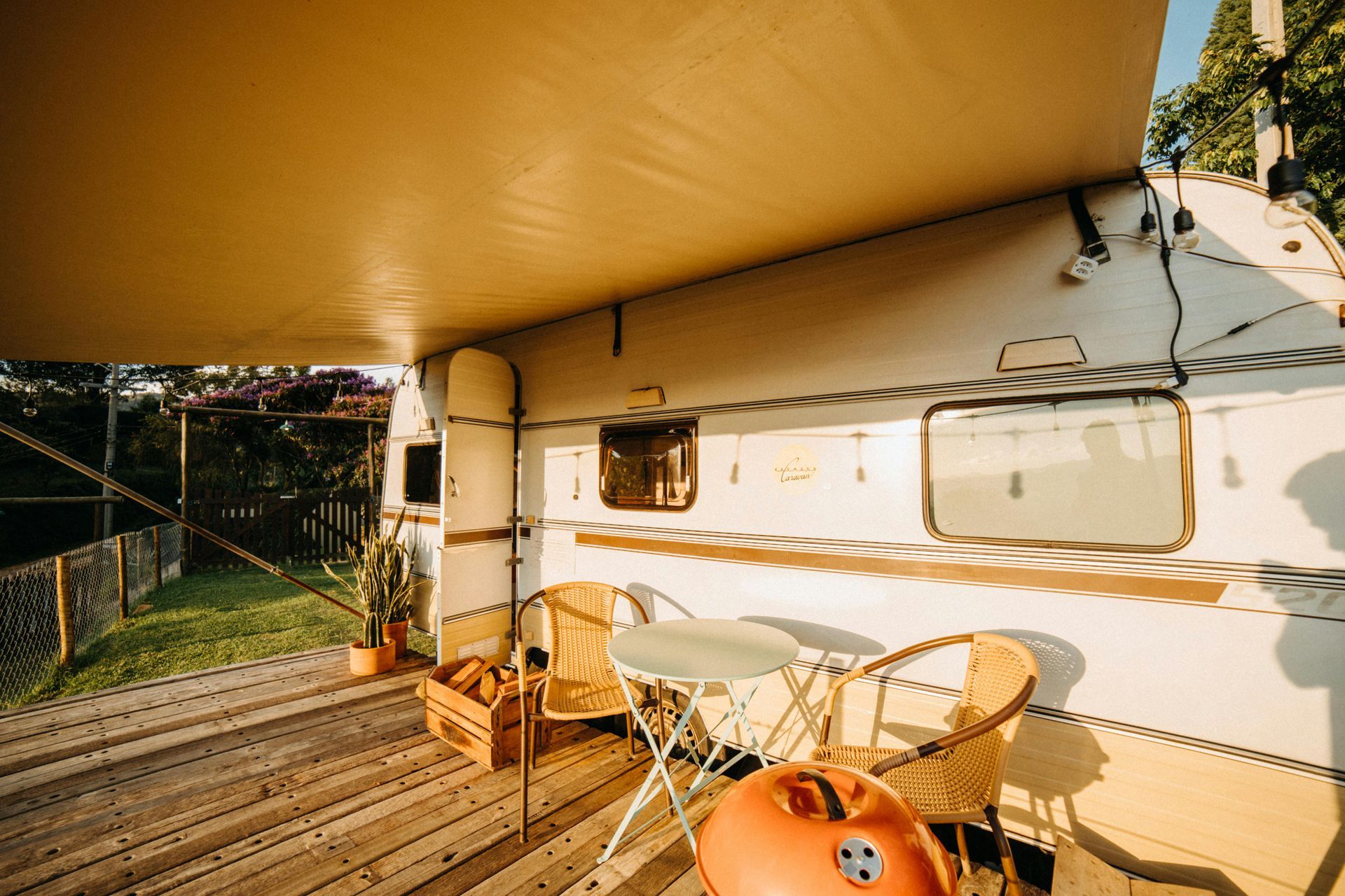White vintage caravan with outdoor seating on a wooden deck, beneath an awning.