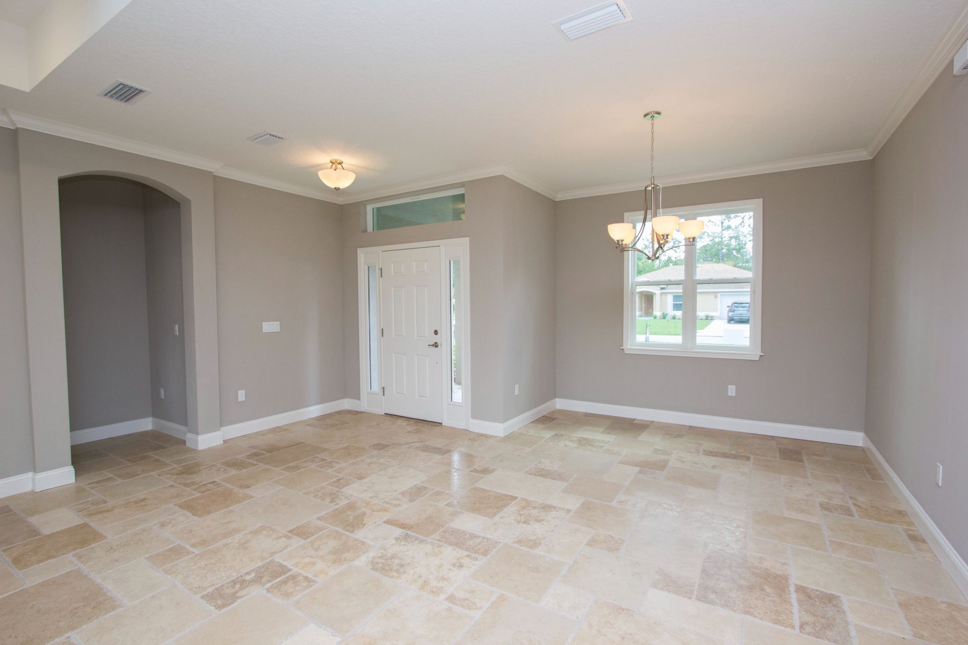 Empty beige living room with tiled floor, white trim, arched doorway, and a window letting in daylight