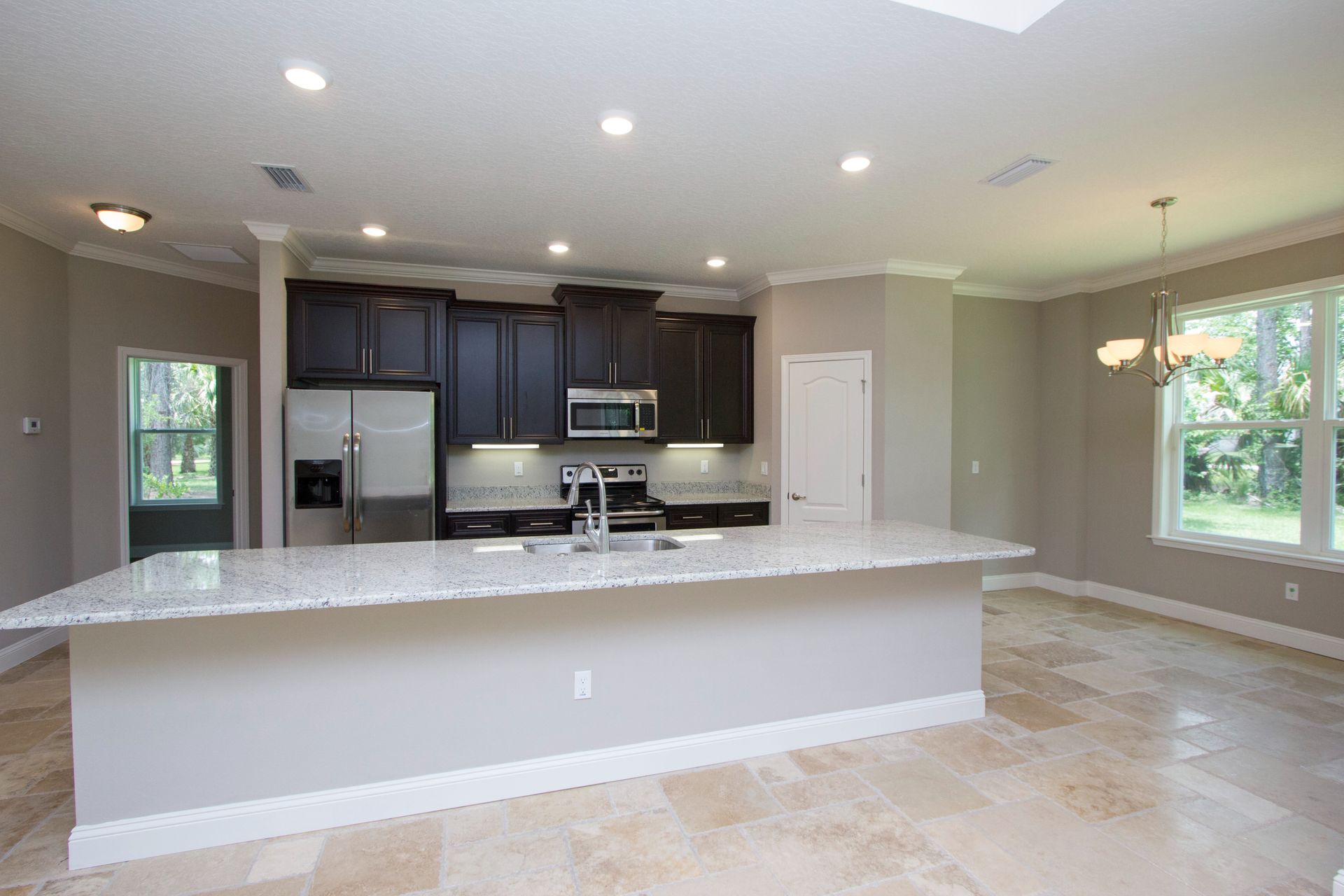 Bright modern kitchen with large island, dark cabinets, granite counters, and open dining area