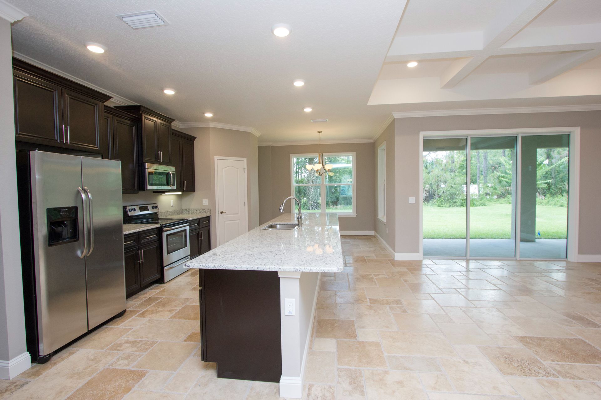 Modern kitchen with stainless steel appliances, large island, and sliding glass doors to a backyard