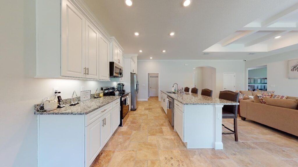 Bright open kitchen and living area with white cabinets, island seating, and beige sofa