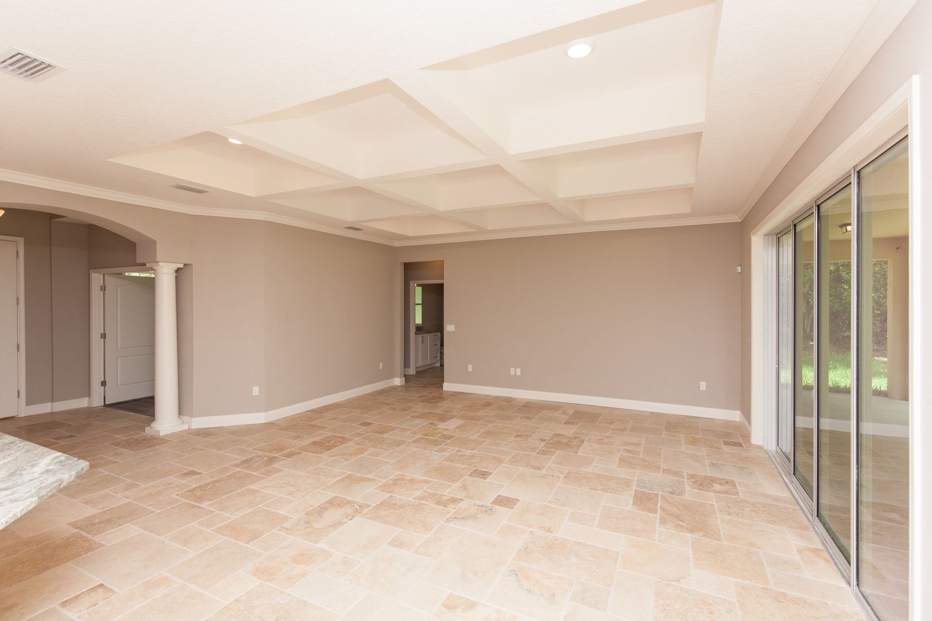 Empty beige living room with tiled floor, recessed ceiling, and sliding glass doors to the patio