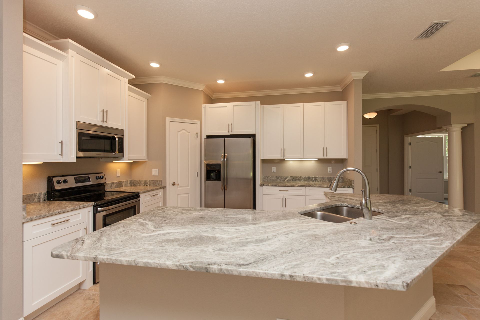 Bright modern kitchen with white cabinets, stainless appliances, and a large marble island.