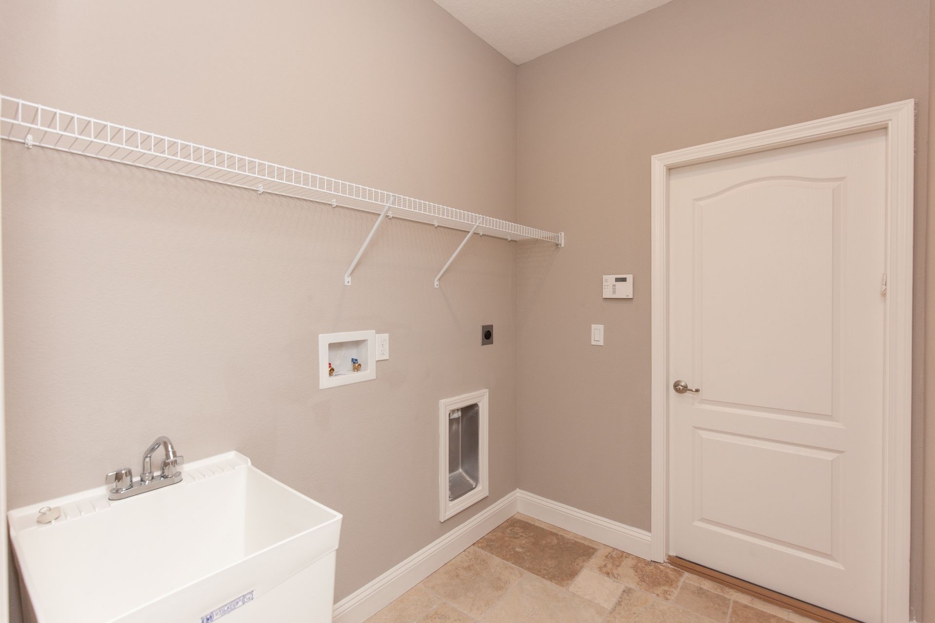 Empty laundry room with beige walls, white shelving, utility hookups, and a closed door