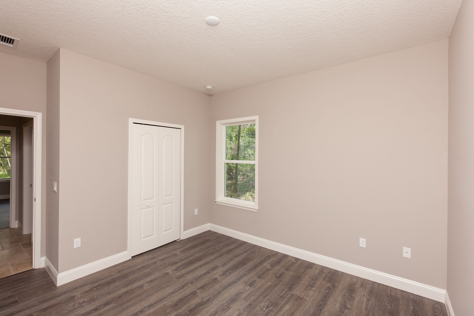 Empty beige bedroom with a closet, window, and wood-look flooring