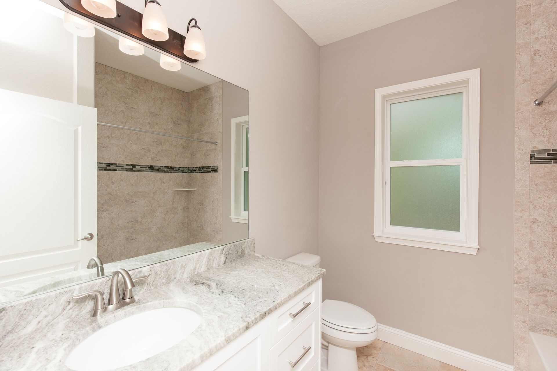 Bright modern bathroom with a vanity, mirror, shower, and frosted window
