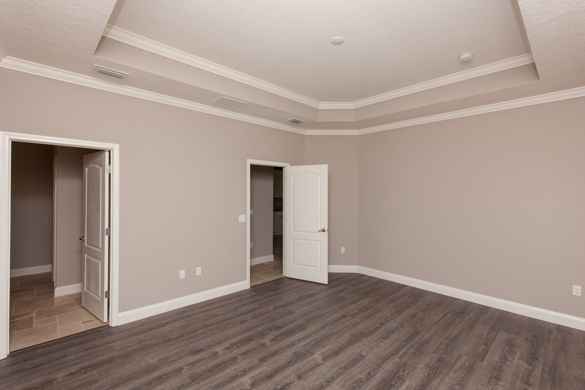 Empty beige bedroom with gray wood flooring, white trim, and two open doors.