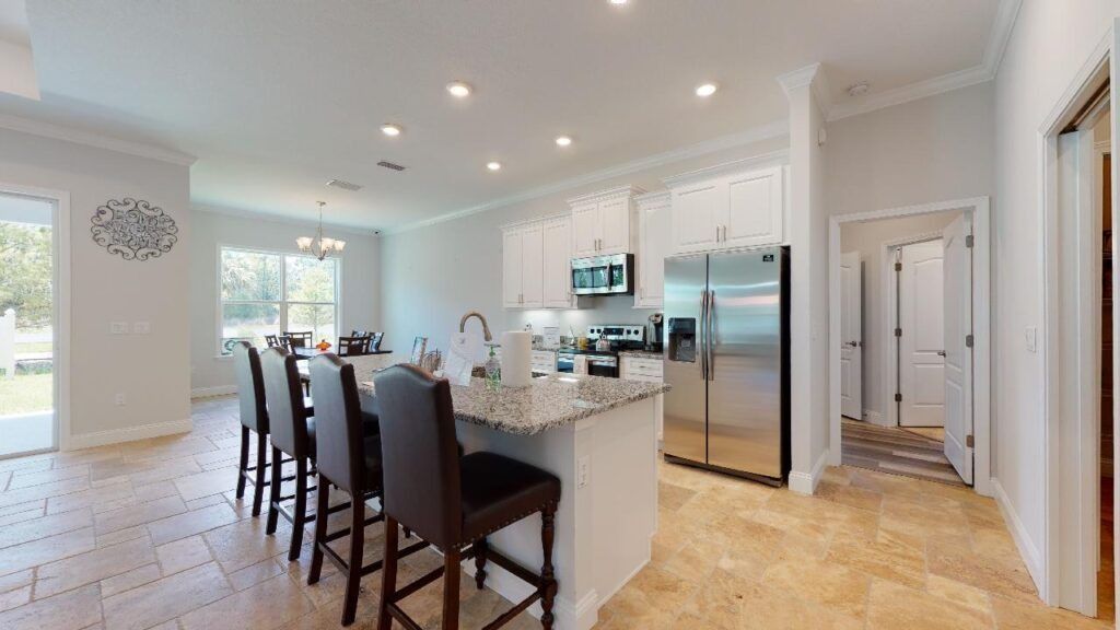 Bright modern kitchen with white island, dark bar stools, stainless fridge, and tiled floor