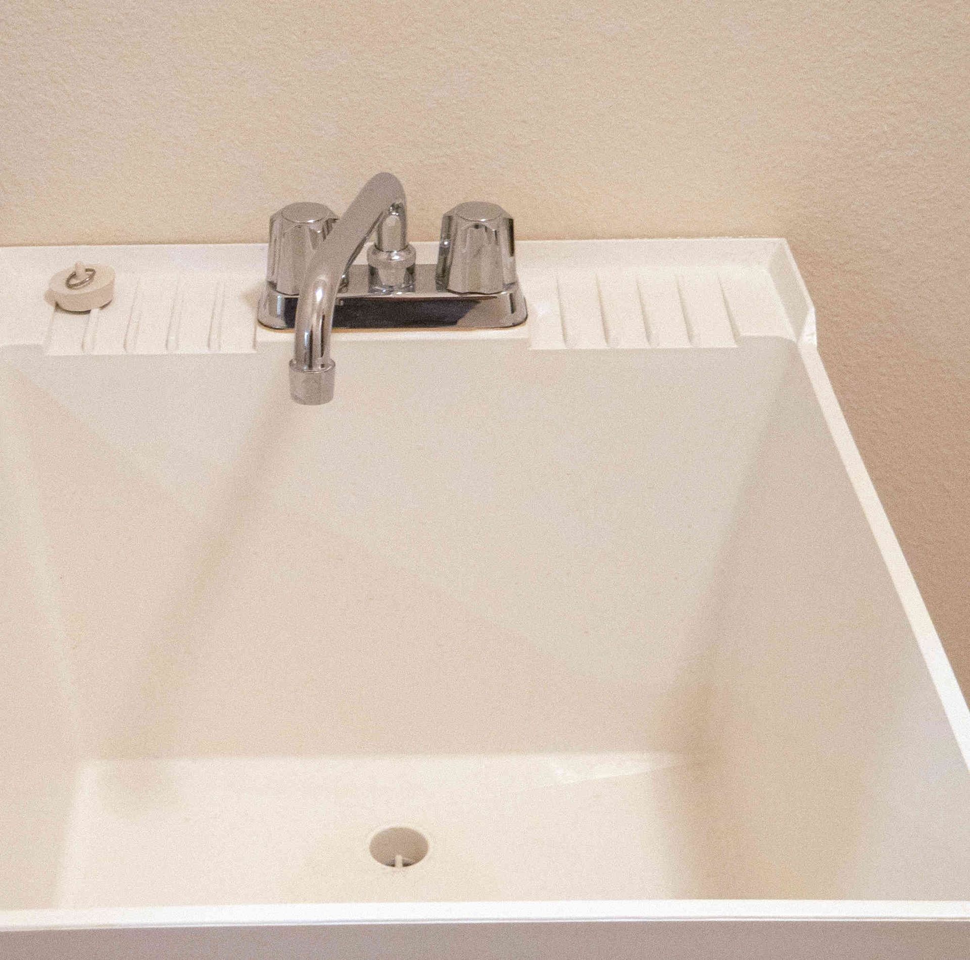 White utility sink with chrome faucet and drain, built into a countertop against a beige wall
