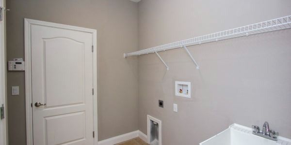Empty laundry room with white door, wall shelf, washer/dryer hookups, and utility connections.
