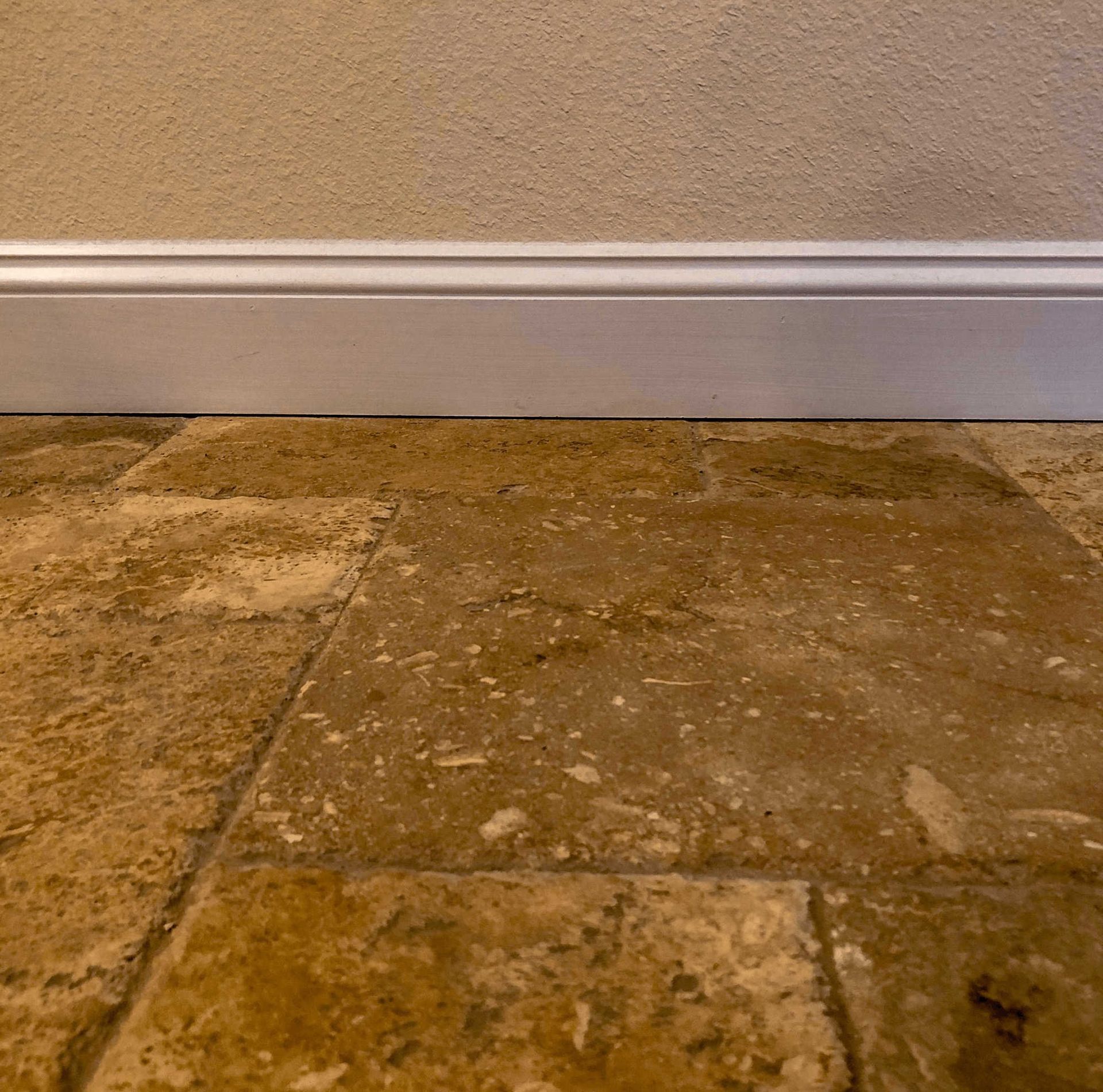 Tan stone tile floor meeting a beige wall with white baseboard trim