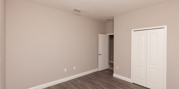 Empty beige bedroom with gray carpet and white closet doors
