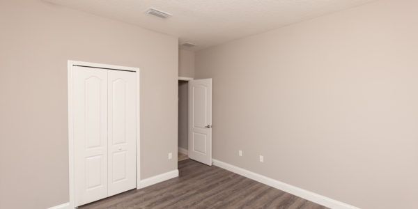 Empty beige bedroom with white double closet doors and a doorway on wood flooring