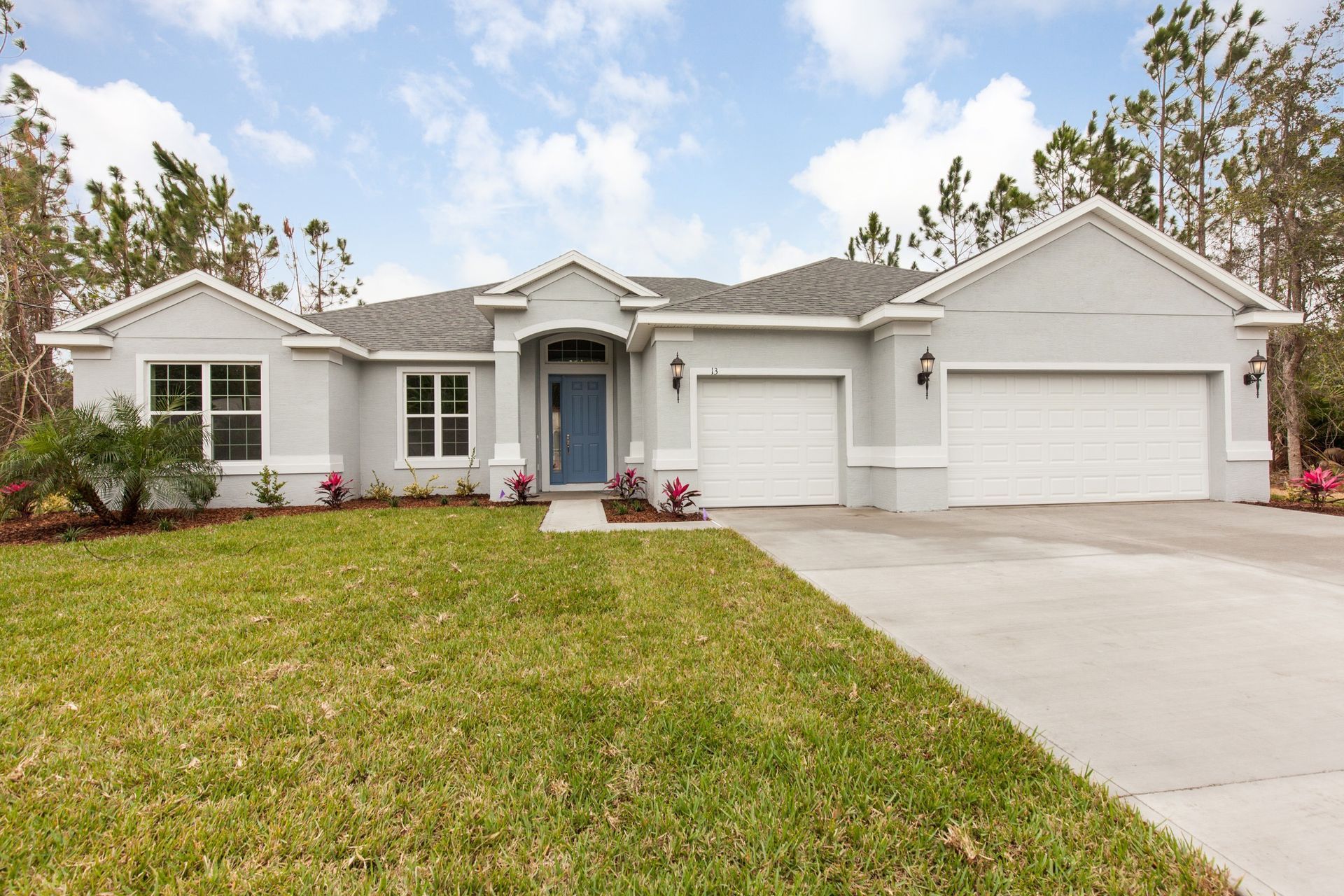 Single-story white house with a two-car garage and a front lawn under a partly cloudy sky