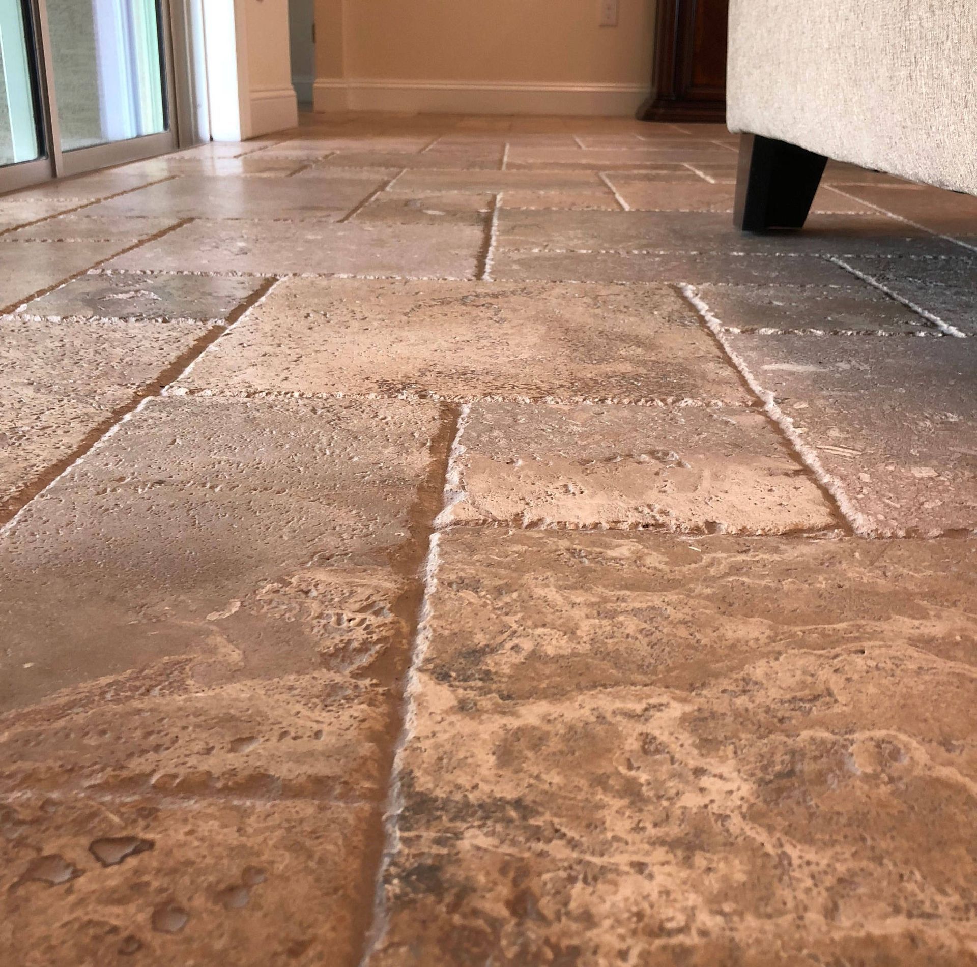 Low-angle view of a tiled hallway floor with beige stone tiles and a doorway in the background