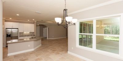 Bright open kitchen and living area with tiled floor, white cabinets, and large windows overlooking a grassy yard.
