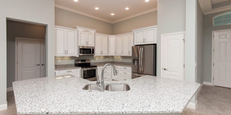 Bright modern kitchen with white cabinets, granite island, and stainless steel appliances