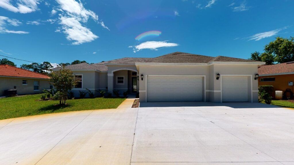Single-story suburban house with a three-car garage and a wide concrete driveway under a blue sky.