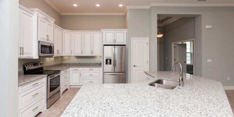Bright modern kitchen with white cabinets, stainless appliances, and a large marble island with sink