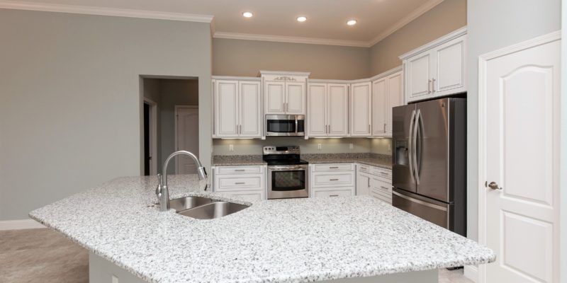 Bright modern kitchen with white cabinets, stainless appliances, and a large speckled island counter