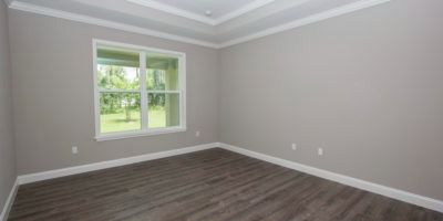 Empty gray bedroom with dark wood floor and a window overlooking green trees