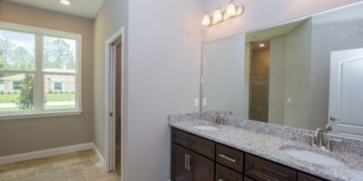 Modern bathroom vanity with granite countertop and mirror, beside a bright window view into a neighboring room.