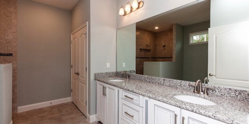 Bright bathroom with white cabinets, granite countertop, sink, mirror, and walk-in shower.