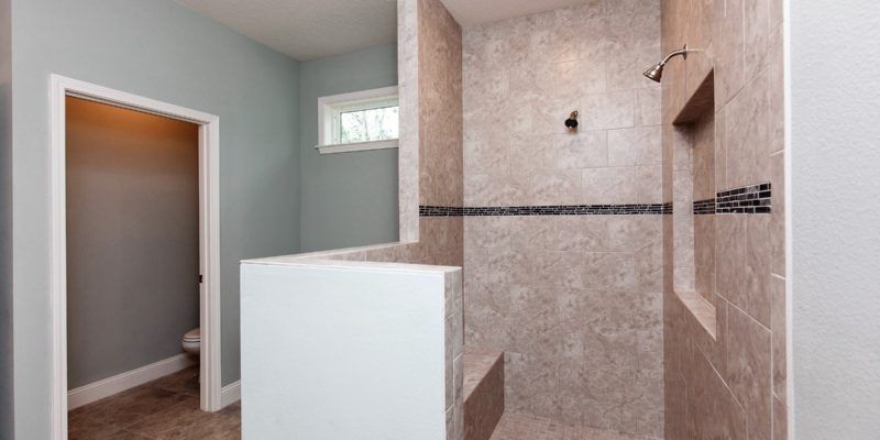 Empty modern bathroom with tiled shower, white half wall, and small window.