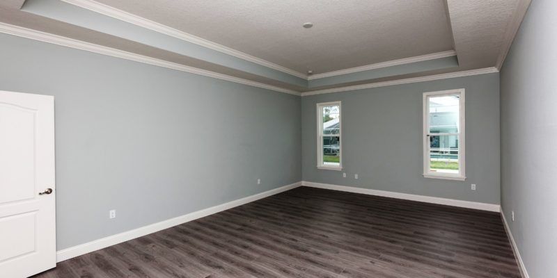 Empty gray bedroom with dark wood floors, white trim, and two windows