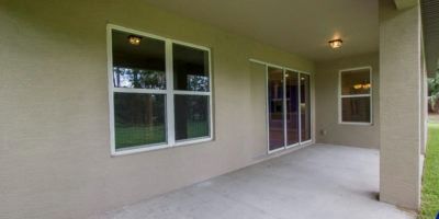 Covered apartment patio with beige walls, windows, and sliding glass doors under a roofed overhang.