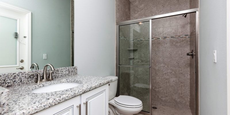 Modern bathroom with granite vanity, mirror, glass shower, and toilet in a neutral gray and white color scheme