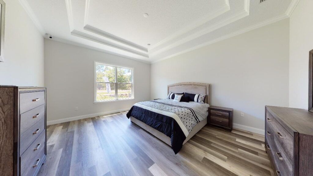 Bright modern bedroom with a bed, dressers, light wood floors, and a window letting in daylight