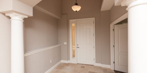Empty beige hallway with white trim, columns, and front door, lit by a ceiling light