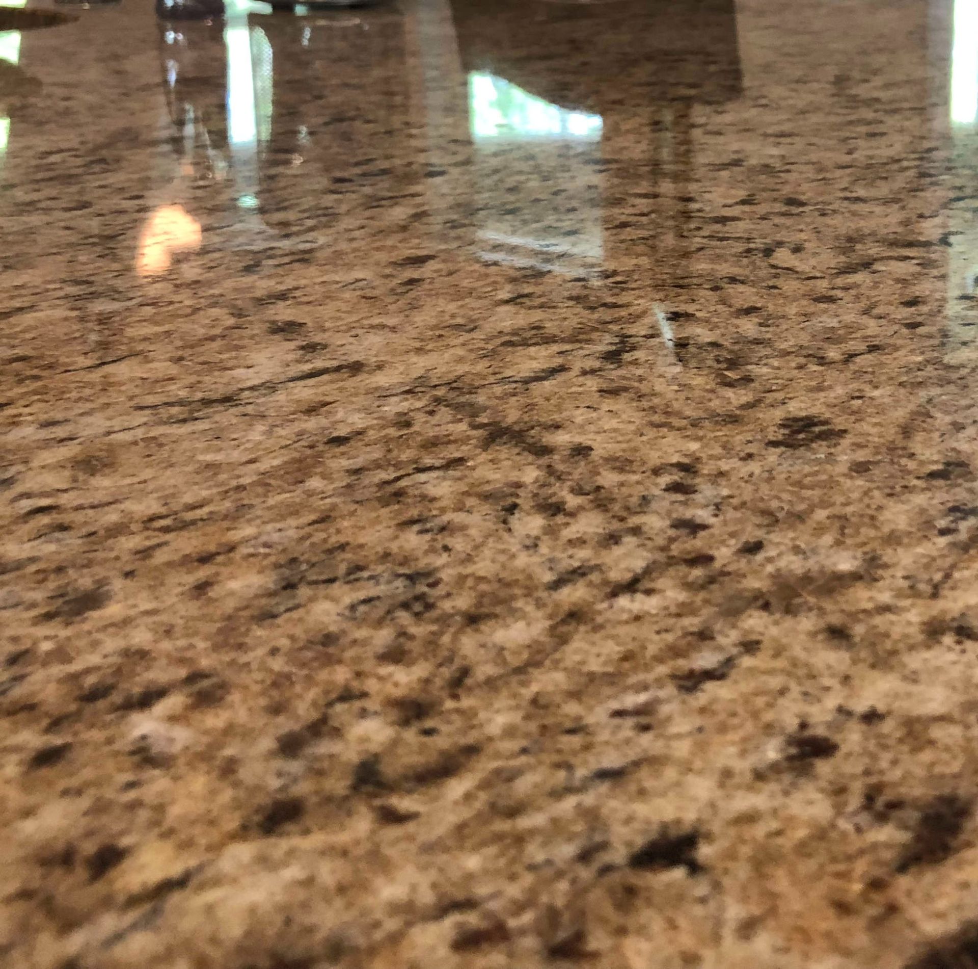 Close-up of a polished granite countertop with brown, black, and beige speckles and light reflections