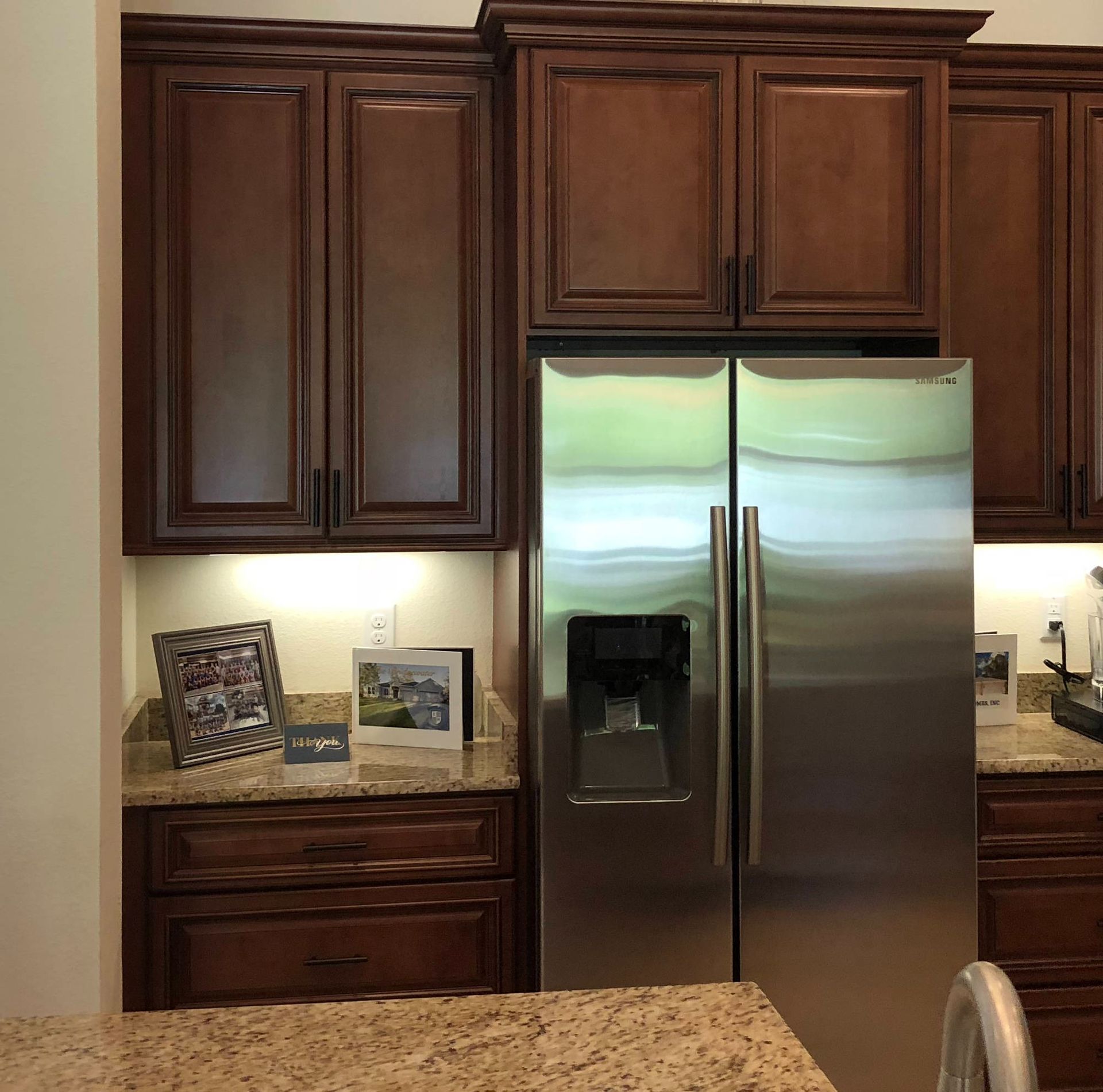 Dark wood kitchen cabinets above a stainless steel French-door refrigerator and granite countertop.
