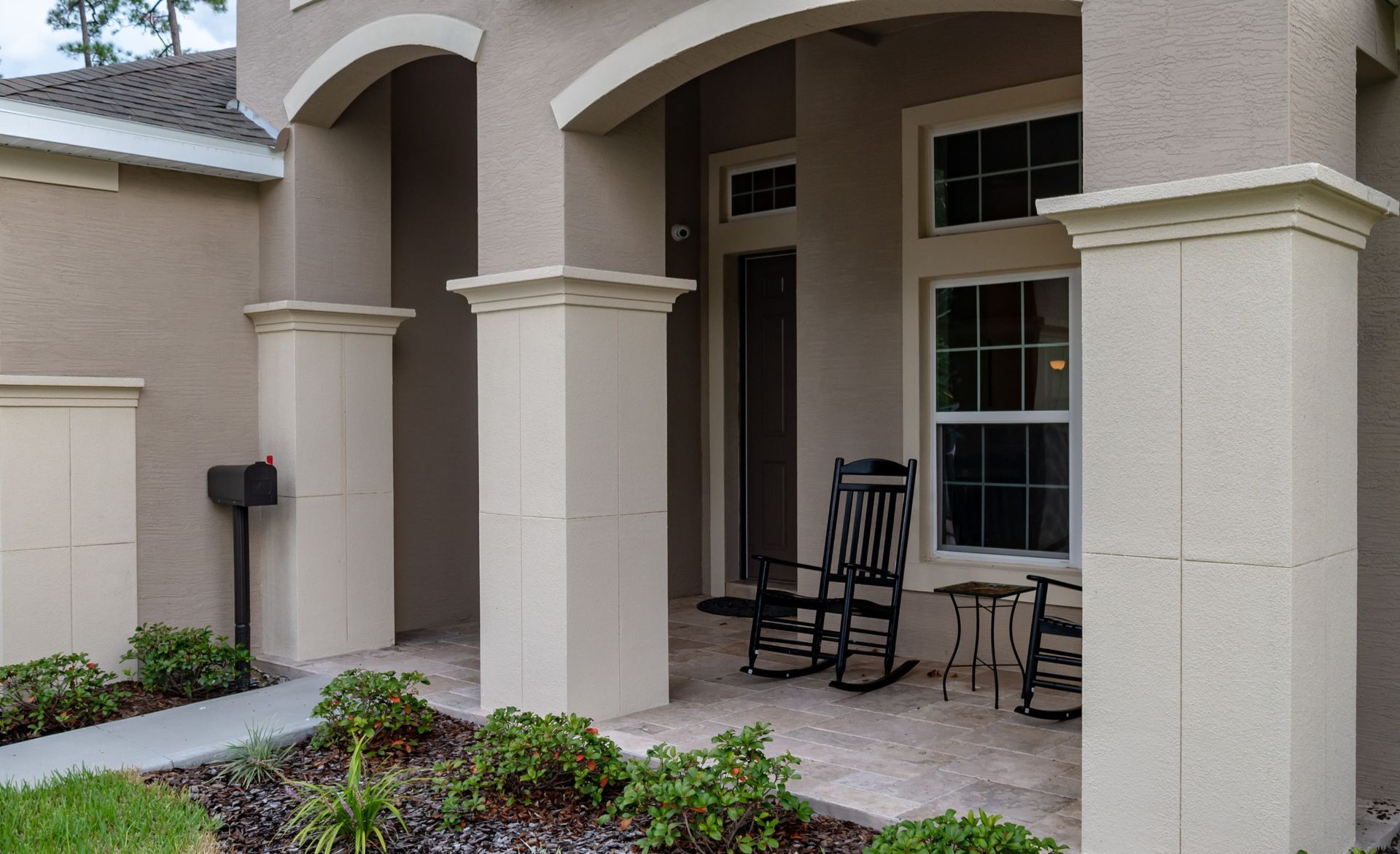 Front porch with stucco columns, chairs, and potted plants beside a house entrance
