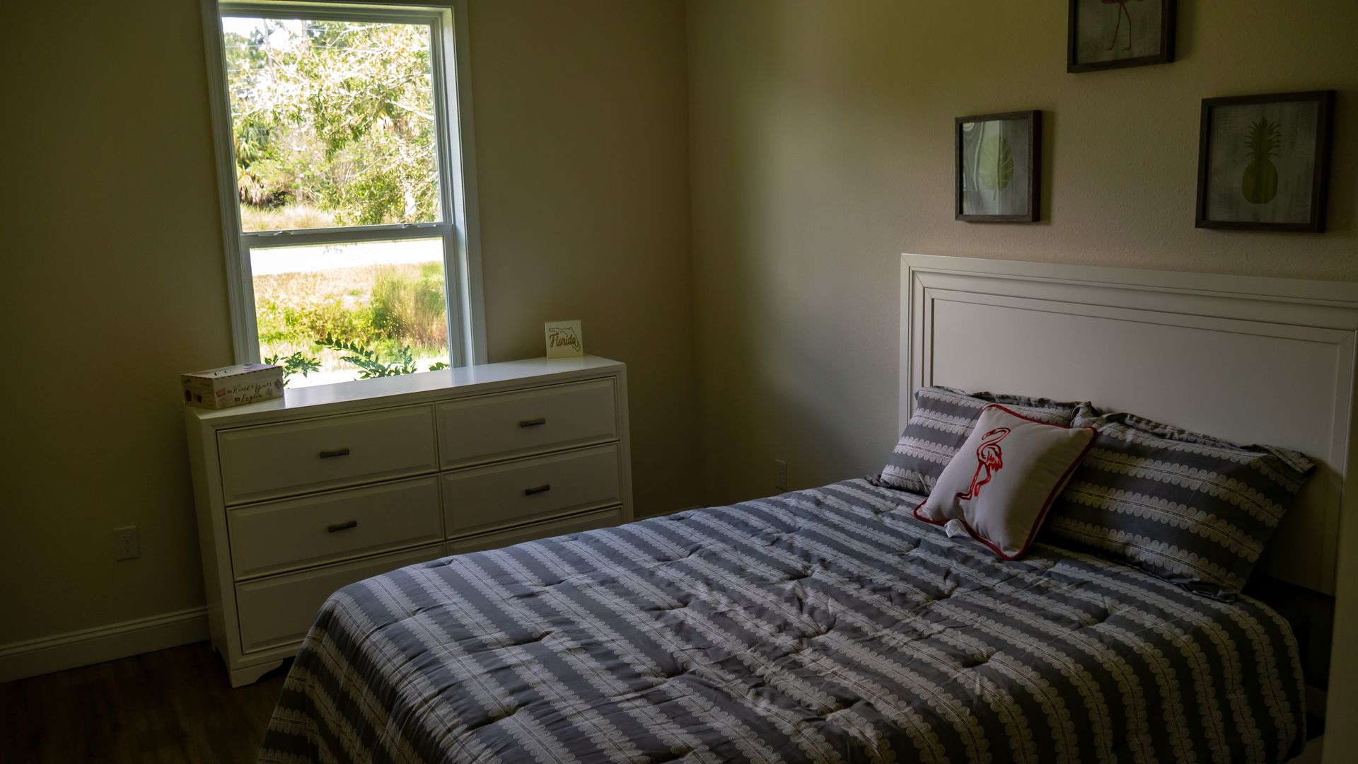 Small bedroom with a striped bedspread, white dresser, and window with daylight.