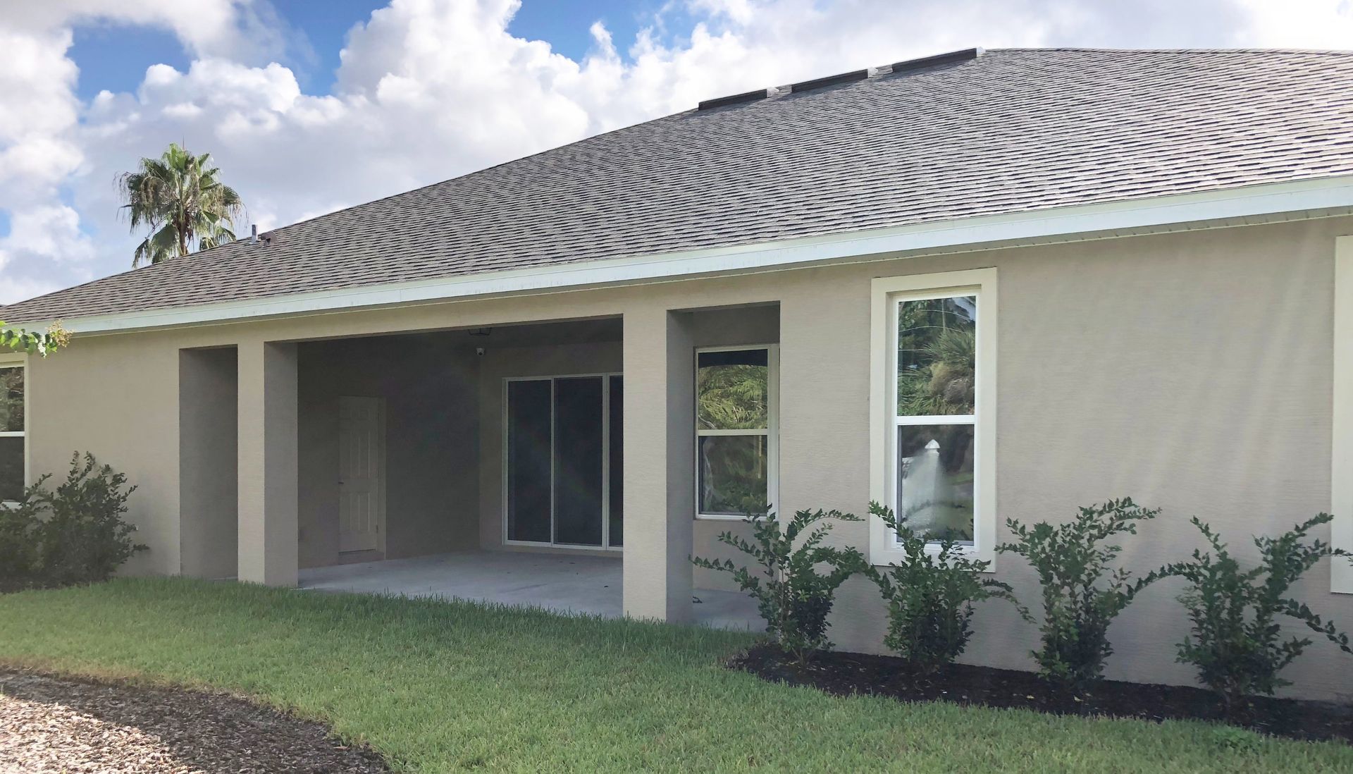 Single-story house with screened porch, light exterior walls, and a striped roof in a sunny yard.