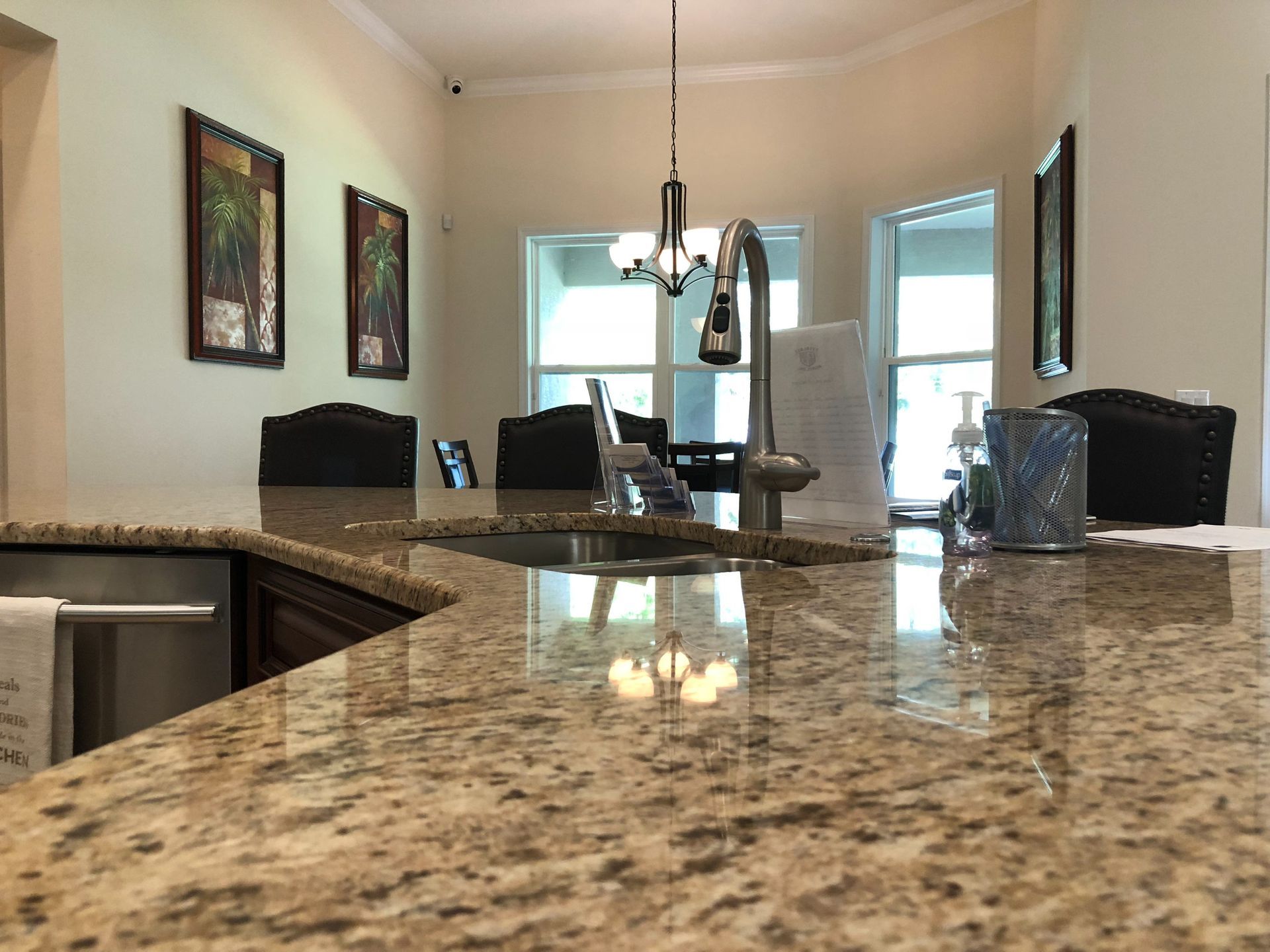 Modern kitchen with granite countertop, black chairs, pendant light, and bright windows.
