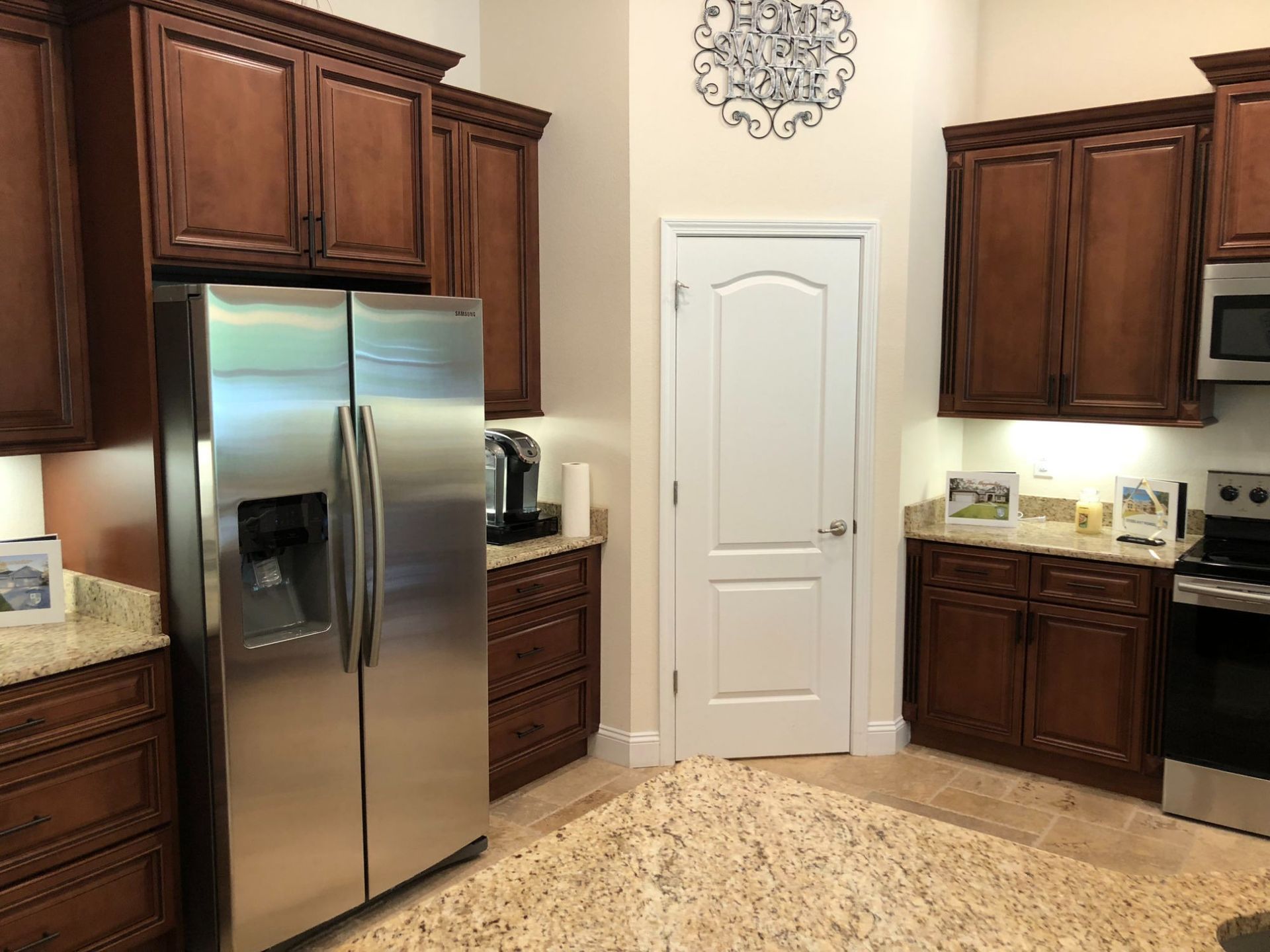 Kitchen with stainless steel fridge, dark wood cabinets, white door, and beige tile floor.