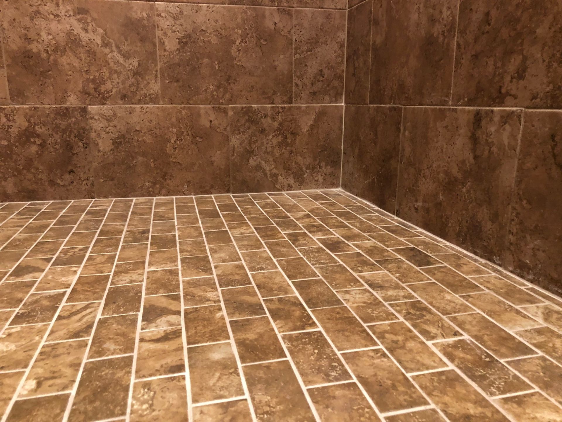 Empty brown tiled shower corner with floor and walls.