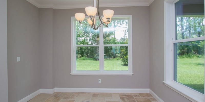 Empty beige dining room with chandelier and large windows overlooking a green yard