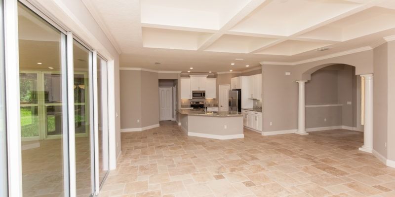 Spacious empty living room with beige tile floors, white cabinetry, and large sliding glass doors