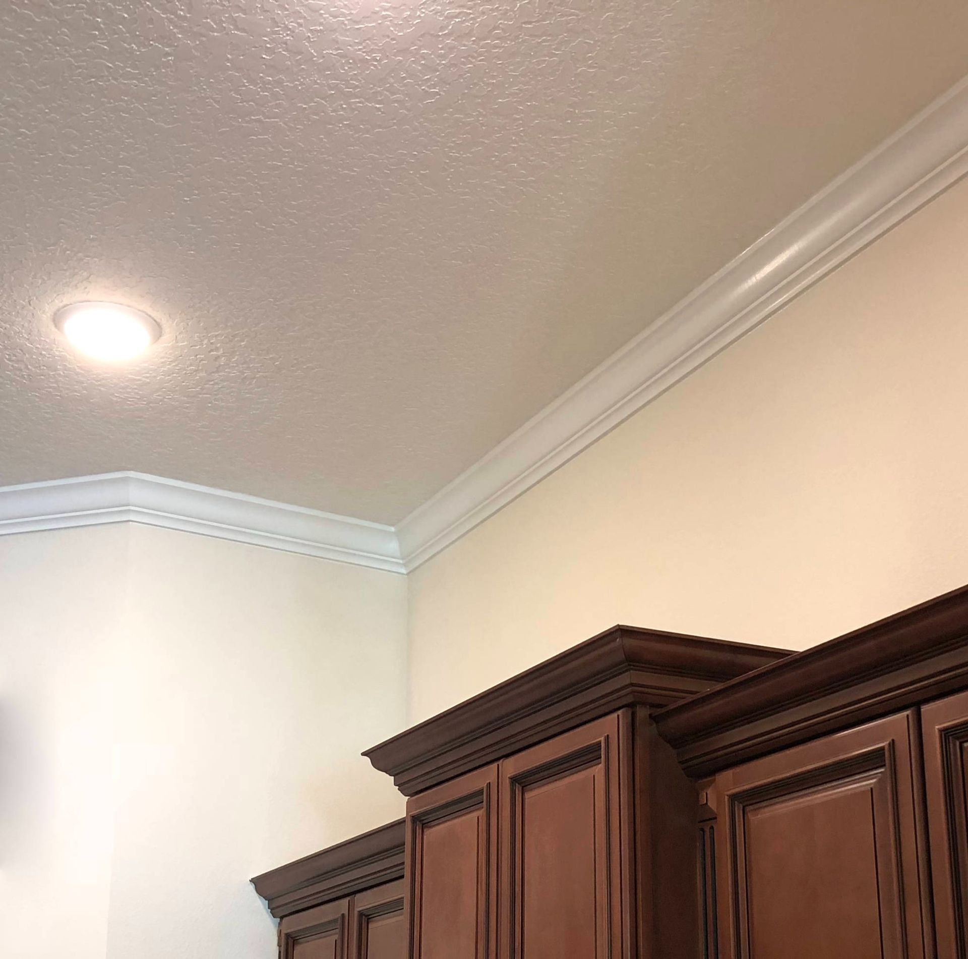 Corner of a room with white crown molding, recessed light, and dark wood cabinets against beige walls