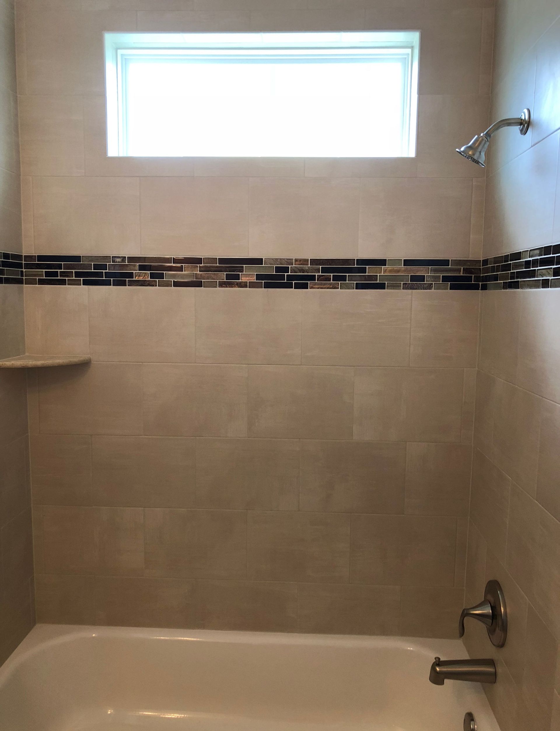 Bathroom shower with beige tile walls, a dark mosaic border, window, and tub faucet and showerhead.