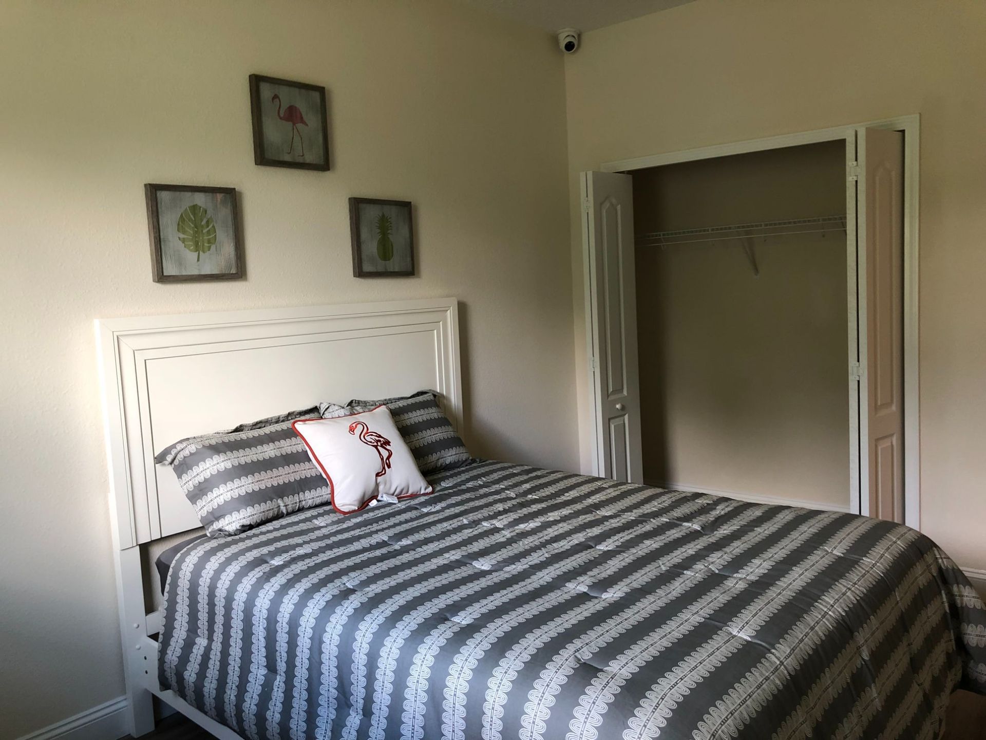 Neatly made bed with striped bedding in a simple bedroom, beside an open closet and wall art.
